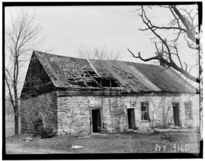 Black and white photo of delapidated one story building with broken roof