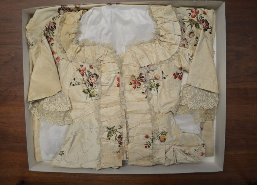 Archival box displaying folded up ivory dress with enboded flowers and berries